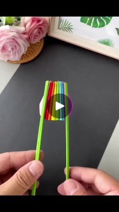 someone is holding two colorful straws in front of a flower pot and a framed photo