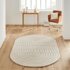 a living room with a chair, table and rug on the wooden floor next to a window