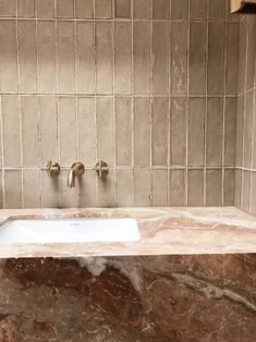 a marble sink with two faucets on the wall and brown tile behind it