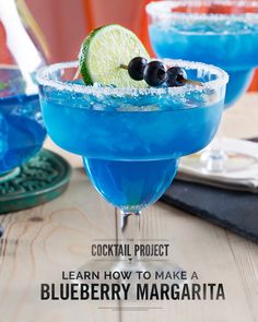 two blue margaritas sitting on top of a wooden table