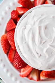 a white bowl filled with whipped cream and strawberries on top of a blue table