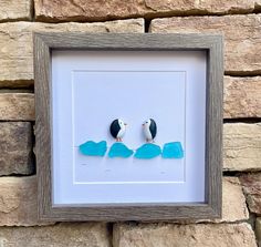 two small birds sitting on top of a blue piece of paper in a wooden frame