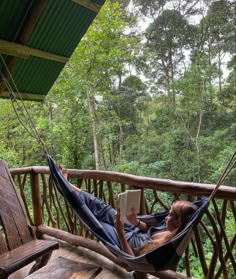 a person laying in a hammock reading a book on a porch with trees in the background