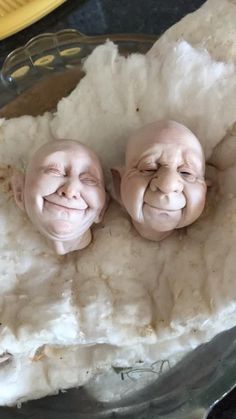 two baby trolls are sitting in a glass bowl on a counter top, one is smiling and the other has its eyes closed