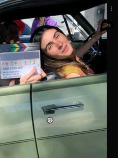 a woman sitting in the driver's seat of a car holding up a movie clapper