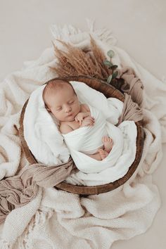 a newborn baby is curled up in a basket on a white blanket with dried grass