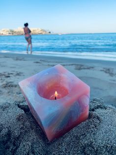 a candle sitting on top of a sandy beach next to the ocean with a person in the background