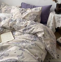 an unmade bed with purple and white comforter, pillows and books on it