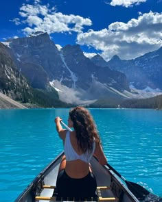 a woman in a canoe paddling on the water with mountains in the background and clouds in the sky