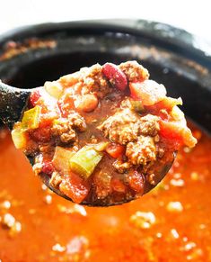 a ladle full of chili and meat soup is being held up by a spoon