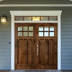 two wooden doors on the side of a gray house with white trim and wood flooring