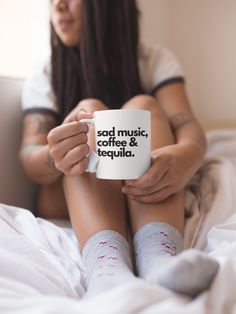 a woman is sitting on her bed holding a coffee mug that says good music, coffee & tequila