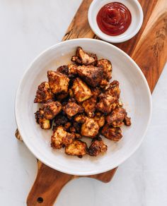 a white bowl filled with tofu next to a wooden cutting board and ketchup