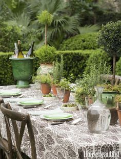 the table is set with green plates and vases filled with greenery, surrounded by potted plants