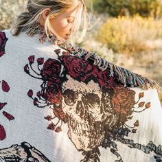 a woman wearing a white and red blanket with skulls on it in the middle of a desert