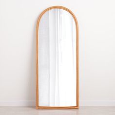 an oval wooden mirror on the floor in front of a white wall with curtains behind it