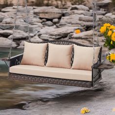 a swing bed with four pillows on it next to water and flowers in the background