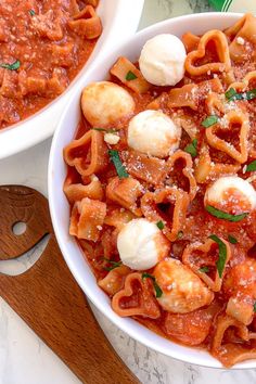 two bowls filled with pasta and sauce on top of a marble counter next to a wooden spatula