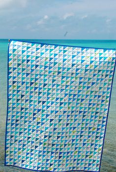 a blue and white quilt sitting on top of a sandy beach next to the ocean