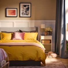 a bed with yellow sheets and pillows in a bedroom next to two pictures on the wall