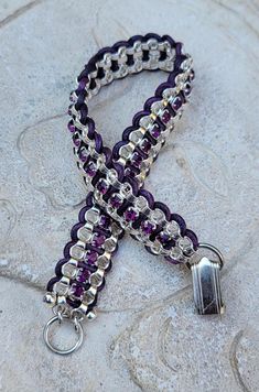 a close up of a purple and silver ribbon with a metal clasp on a rock