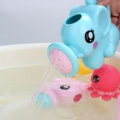 a child's hand is pouring water into a bathtub with an elephant toy