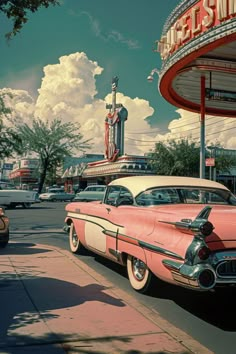 an old pink and white car parked in front of a movie theater