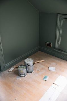 two paint cans sitting on top of a hard wood floor next to a window in an empty room