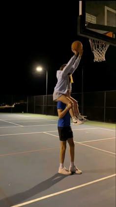 two people are playing basketball on an outdoor court at night with lights in the background