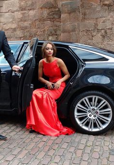 a woman in a red dress is sitting in the open door of a black car