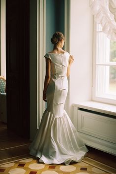 a woman standing in front of a window wearing a white dress with ruffles on the skirt