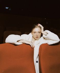 a woman sitting on top of a red couch covered in a white robe and holding her hand to her head