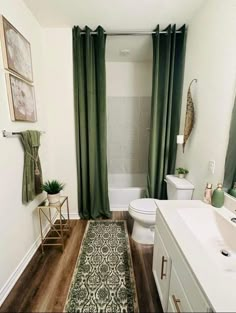 a white bathroom with green curtains and rugs on the floor, along with a toilet