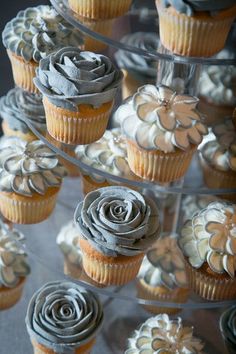 cupcakes with frosting and flower decorations are arranged on a clear cake stand