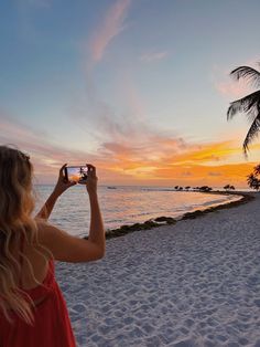 a woman in a red dress taking a photo on the beach