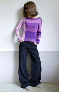 a woman standing in front of a wall with her hands on her hips wearing wide jeans and a purple sweater