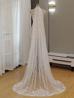 a white wedding veil on a mannequin in front of a window with curtains