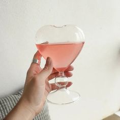 a person holding up a wine glass with pink liquid in the shape of a heart