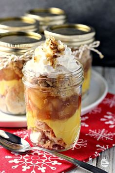 three jars filled with dessert sitting on top of a red and white table cloth next to silverware