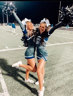 two cheerleaders are dancing on the football field at night with their hands in the air