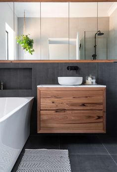 a white bath tub sitting next to a bathroom sink under a large mirror on top of a wooden cabinet