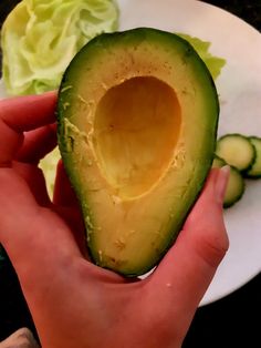 an avocado is being held in front of a plate with lettuce