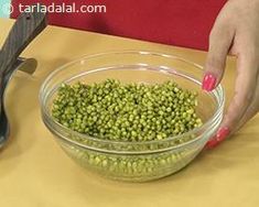 a woman is scooping peas into a bowl with a pair of scissors on the table