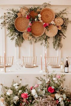 an arrangement of flowers and candles on a table with wicker baskets hanging above it