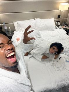 a man and woman laying in bed with their hands up to the ceiling, making funny faces