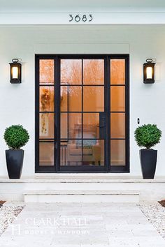 two large black vases with plants in them on the side of a white house