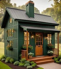 a small green house with a porch and steps leading up to the front door that is covered in potted plants