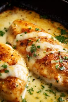 two pieces of chicken covered in cheese and parsley on top of a skillet