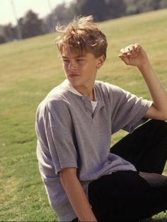 a young man sitting on the ground with his hands behind his head and looking off to the side