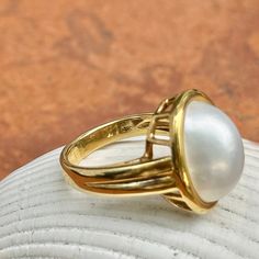 New, but old pieces, never worn, recently acquired from a premier jeweler located in Minneapolis, MN for many years- a rare opportunity! 18KT yellow Ggld genuine, bezel-set, white, oval, mabe pearl ring. Size 6.75 Sizable by us for a fee or your local jeweler Weight: 10.3 grams Band width: 3mm in back Pearl measures: 15mm x 11mm oval mabe pearl Stamped 18k By Honora Elegant White Domed Rings, Elegant White Domed Jewelry, Classic White Gold Cabochon Jewelry, Timeless Gold Dome Ring With Cabochon, Timeless Oval Cabochon Jewelry, Classic Oval Cabochon Dome Ring With Polished Finish, Yellow Gold Cabochon Pearl Ring For Gift, Yellow Gold Cabochon Pearl Ring As Gift, Oval Cabochon Dome Ring For Anniversary